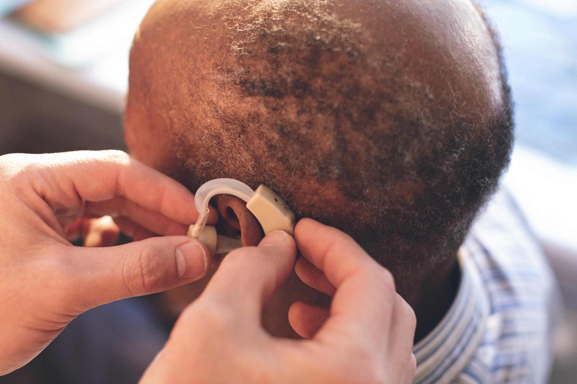 Hight angle view of caucasian male doctor applying hearing aid to African senior man ear in clinic