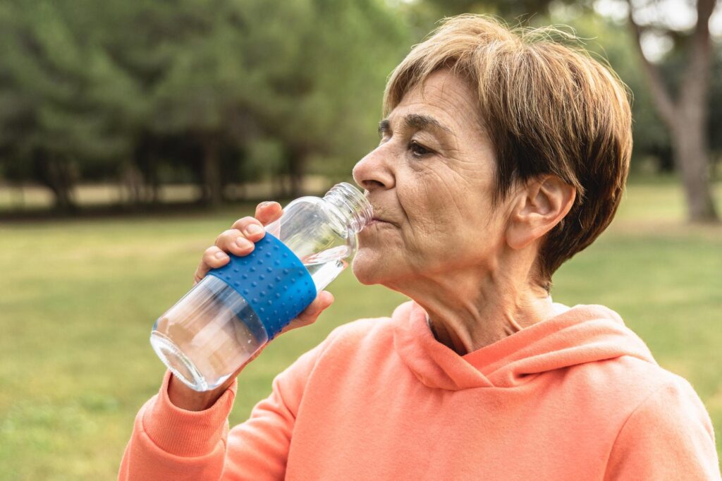 Senior woman drinks water after jog routine outdoor at city park - Elderly exercise and healthy life